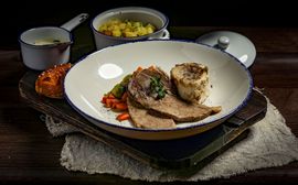 Tafelspitz served in a pot with side dishes such as root vegetables, hash browns and chive sauce.