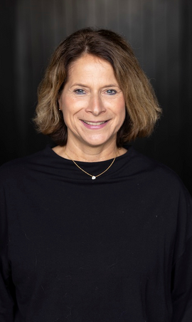 Portrait of a smiling woman with shoulder-length hair against dark backdrop