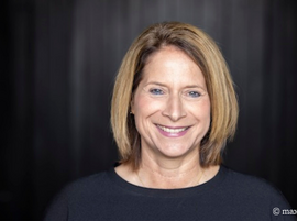 Portrait of a smiling woman with shoulder-length hair against dark backdrop