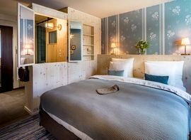 Ein lichtdurchflutetes Musterzimmer im neuen Hotel "Marias Platzl", welches mit einem großen Bett und viel hellem Holz und Farben ausgestattet ist.