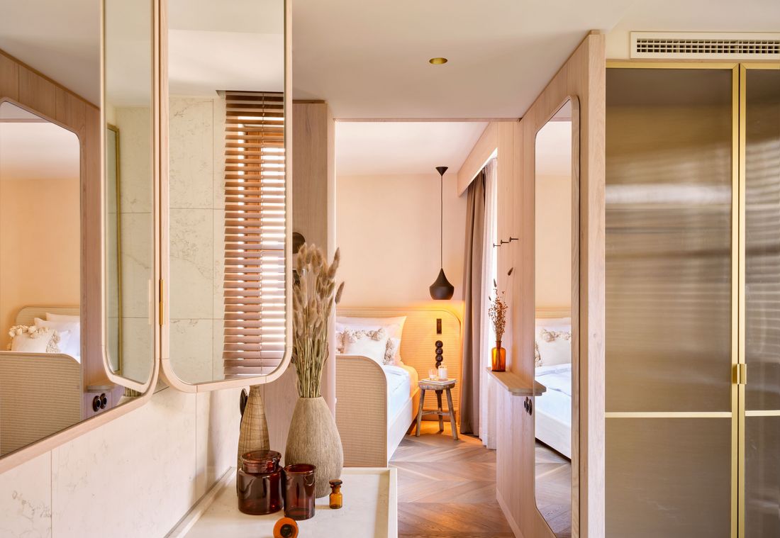 Blick durch das moderne Badezimmer auf einen hellen Schlafbereich in einer Suite in München