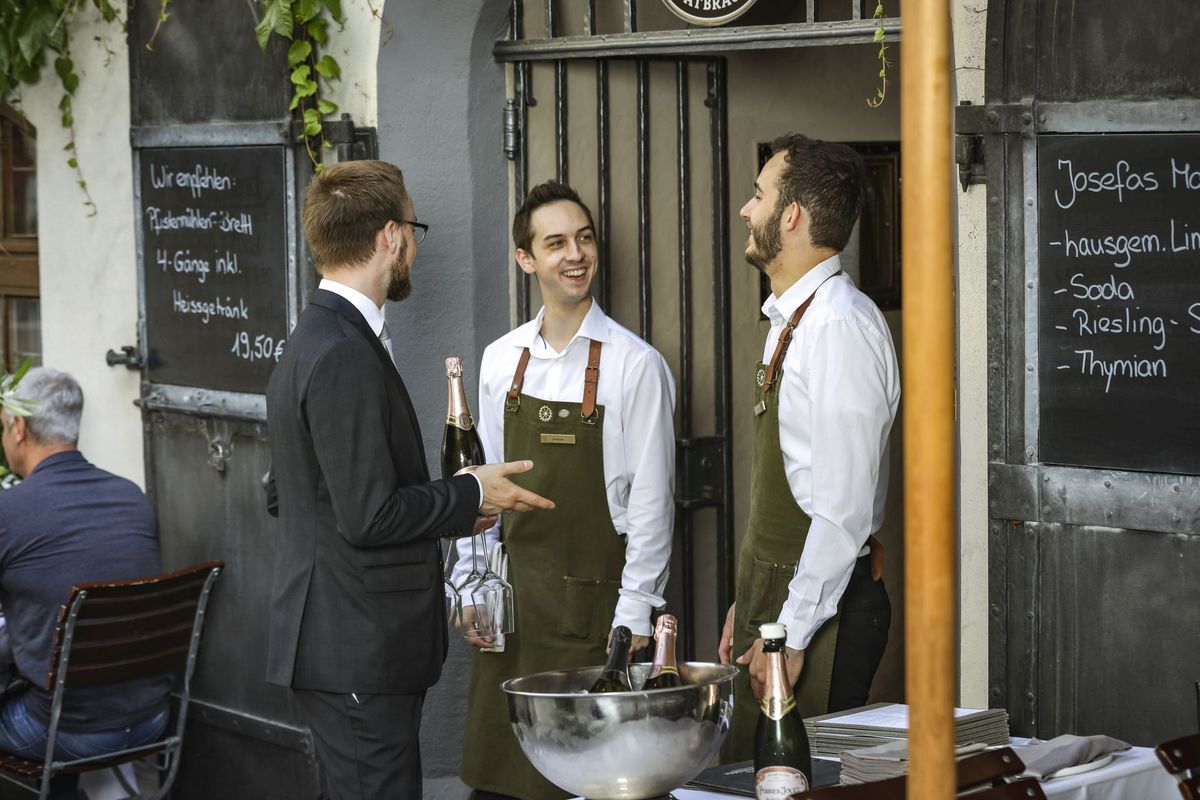 Drei Mitarbeiter des Restaurant Pfistermühle stehen von einem eisernen Tor, das ins innere des Restaurants führt und unterhalten sich.