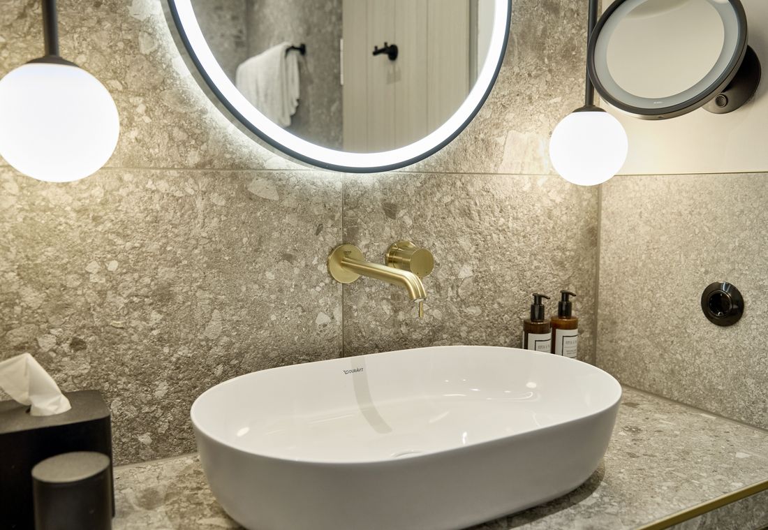 Das stilvolle Bad mit Naturstein-Waschbecken, beleuchtetem Spiegel und eleganten Armaturen schafft eine edle Atmosphäre