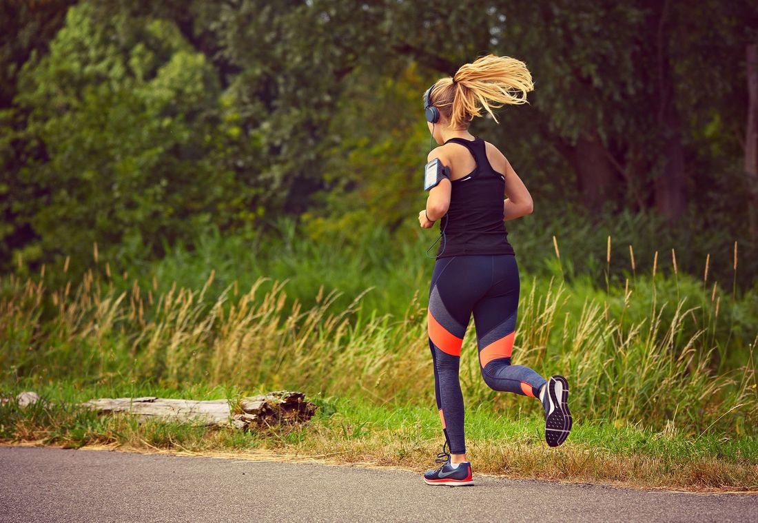 Woman in sportswear jogging on a paved path through green nature