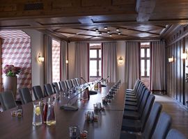 Großer Meetingraum im Tagungshotel in München mit langer Tafel in der Mitte des Raums. Auf dem Tisch sind gefüllte Glaskaraffen und Trinkgläser vorbereitet. 