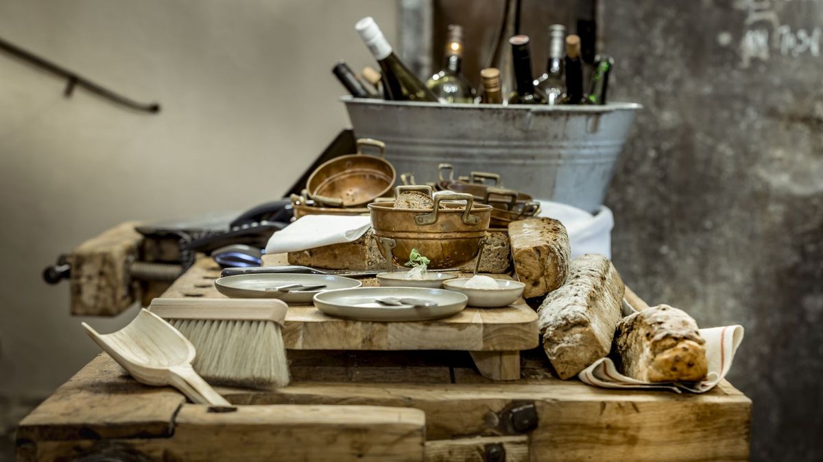 A wooden countertop at the Platzl Hotel in Munich with homemade bread, several plates and bowls, and a zinc tub with various bottles