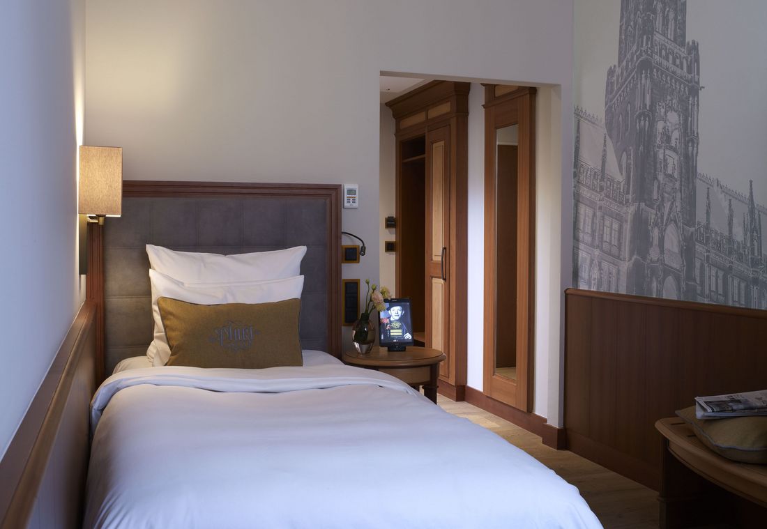 A cozy hotel room with a single bed and a wall art of Munich's town hall in warm tones