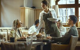 Kellnerin serviert Frühstück in hellem Restaurant mit zufriedenen Gästen