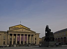 Frontansicht der Münchner Staatsoper bei Abenddämmerung mit vielen Menschen davor