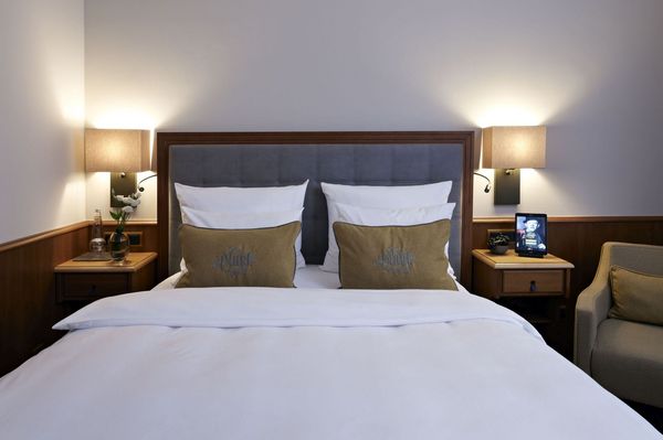 A "classic queen bedroom" in the Platzl Hotel Munich with a queen bed and an armchair next to it