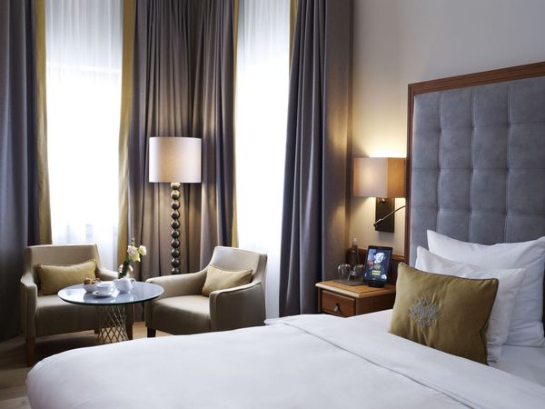 Ein Hotelzimmer in München mit gemachtem Bett, Tisch und Stehlampe im Hintergrund