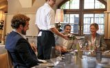 Im Restaurant Pfistermühle am Platzl Hotel München serviert ein Kellner drei Gästen, die an einem Tisch sitzen, einen Weißwein