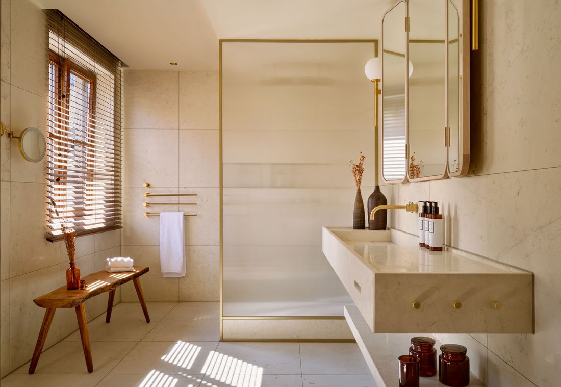 Helles Bad mit Glasduschwand, Messingarmaturen und Naturstein in einer Suite in München