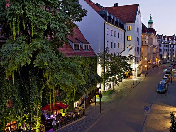 Abendstimmung in der Münchner Altstadt mit gemütlich beleuchtetem Straßencafé und historischen Gebäuden.