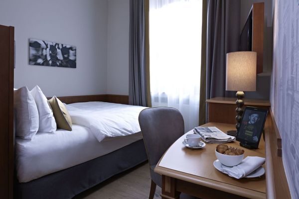 Ein helles "Queenbett Einzelzimmer" im Platzl Hotel München mit einem großen Fenster und Schreibtisch mit Teegedeck