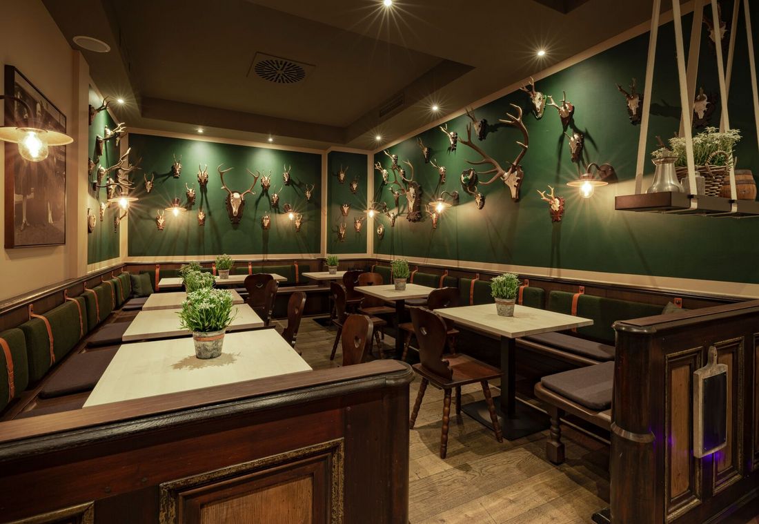 A dining room with antler decor, green walls, wooden furniture, and potted herbs