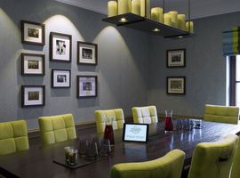 Moderner Meetingraum mit großem Holztisch und 7 grünen Stühlen im Tagungshotel in München. 