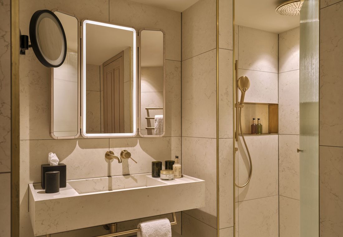 Beleuchtetes Badezimmer mit Spiegel und Regendusche in hochwertiger Suite in München