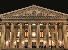 Frontansicht der Münchner Staatsoper bei Abenddämmerung mit vielen Menschen davor
