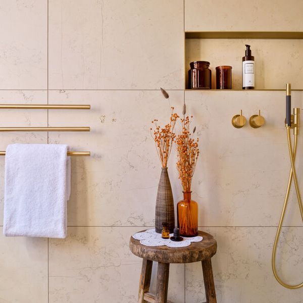 Shower area with golden decoration on marble tiles and flower decorated stool in the foreground.