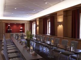 Länglicher Tagungsraum im Tagungshotel München mit in U-Form aufgestellten Tischen. Auf den Tischen sind gefüllte Glaskaraffen und Trinkgläser vorbereitet. 