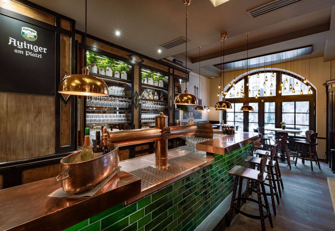 The Ayinger bar features a copper tap, hanging lights, and shelves filled with glasses