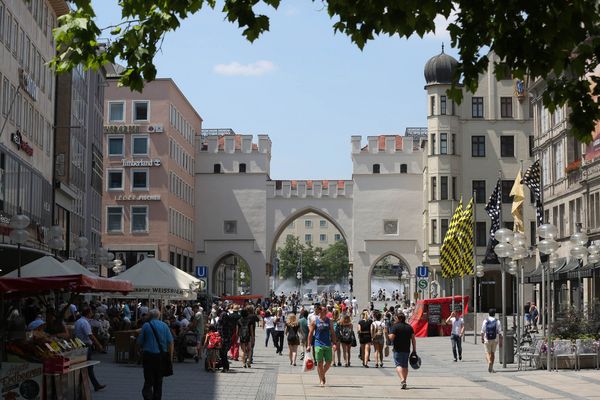 An einem sonnigen Tag spazieren Besucher durch die belebte Fußgängerzone unter dem berühmten Karlstor-Bogen.