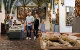 Ein Paar und ein anderer Besucher betrachten die Ausstellungsstücke im Bayerischen Nationalmuseum.