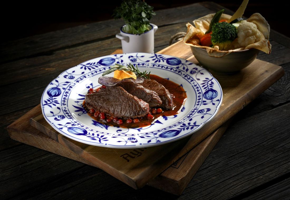 Slices of venison on berry sauce, garnished with rosemary and chips on a blue patterned plate