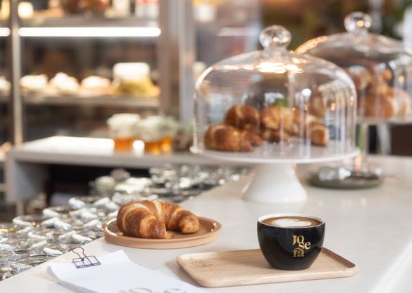 A few croissants and a cappuccino in a cup of the at the Josefa on top of a counter .