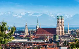 Blick über die Münchner Altstadt mit den Türmen der Frauenkirche vor den Alpen im Hintergrund.