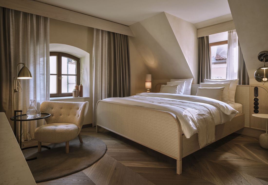 Eine helle Suite in München mit gemütlichem Doppelbett, Sessel und Blick auf charmante Fensterfronten
