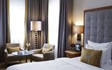 A spacious hotel room at Platzl Hotel Munich with a sitting area with side table and a large bed