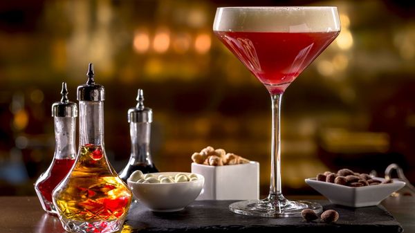 A fancy red cocktail standing on a slate plate in Josefa bar & coffee surrounded by ingredients and small bowls with snacks