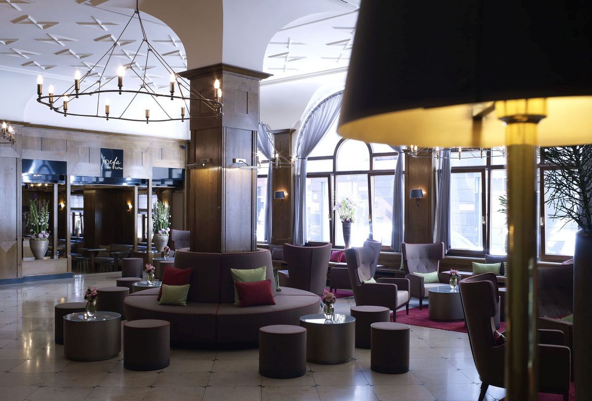 The spacious lobby at the Platzl Hotel Munich with various armchairs and a bench around a column in the middle of the room