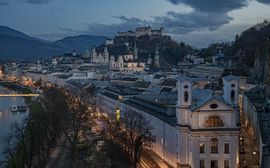 Night view of Salzburg's old town, traversed by the Salzach River and the Hohensalzburg Fortress.