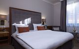 A large bed in a light-filled room at the Platzl Hotel Munich. Directly under the window is a small side table