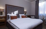 Doppelzimmer Ein großes Bett in einem lichtdurchfluteten Zimmer im Platzl Hotel München. Direkt unter dem Fenster steht ein kleiner Beistelltisch