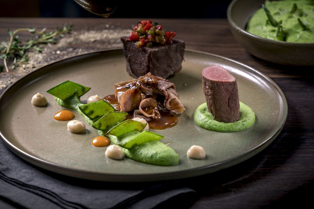 A plate dish with a piece of meat, a herb sauce and sugar snap peas from the kitchen of the Platzl Hotel Munich