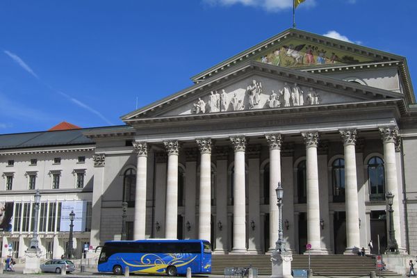 Die Bayerische Staatsoper mit heller Fassade und einem blauen Bus vor den Eingangstüren