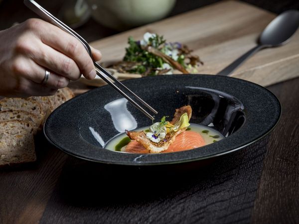 One Chef of the Munich fine dining restaurant arranges a dark plate with a salmon dish with tweezers. 