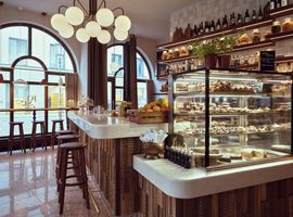 Modern café with large cake display case, wooden counter, stools and high windows at Josefa Bar & Café Munich