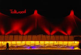 Zelt auf dem Tollwood Winterfestival bei Nacht, mit zwei vorbeischlendernden Personen.