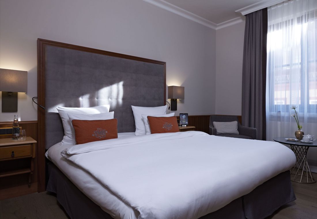 Das einladende Hotelzimmer bietet ein großes Bett mit roten Kissen und edler Holzeinrichtung
