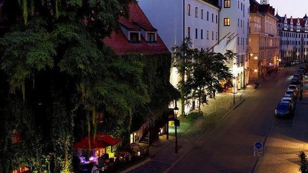 Grün bewachsenes und beleuchtetes Karree Boden & Bar bei Nacht in München