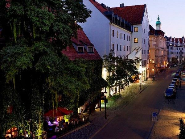 Grün bewachsenes und beleuchtetes Karree Boden & Bar bei Nacht in München