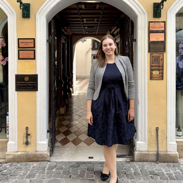 Female staff member welcomes guests at arched entryway with cobblestones and plaques.