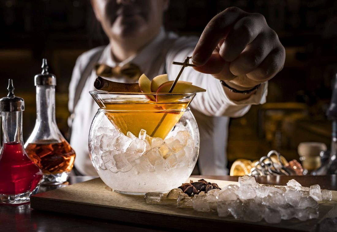 Barkeeper dekoriert Cocktail mit Apfelspalten und Zimt in Eisschale