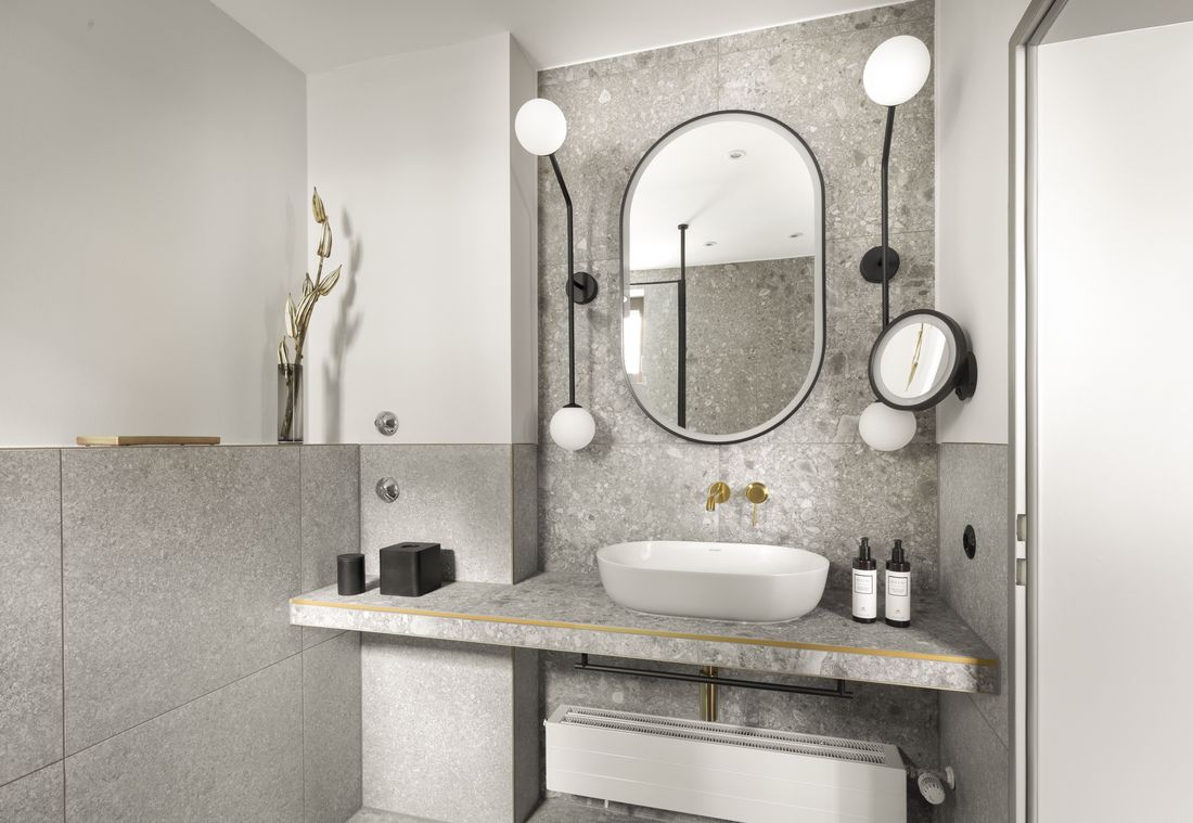 Oval sink with golden faucet, marble top, and round mirror in a modern hotel bathroom