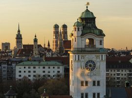 Historischer Kirchturm in München im Hintergrund, weitere Gebäude und Türme bei Sonnenuntergang